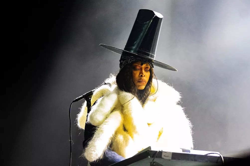 Erykah Badu, seen in a large hat performing in Dallas, has been dragged into the Nicki Minaj/Megan Thee Stallion feud.
